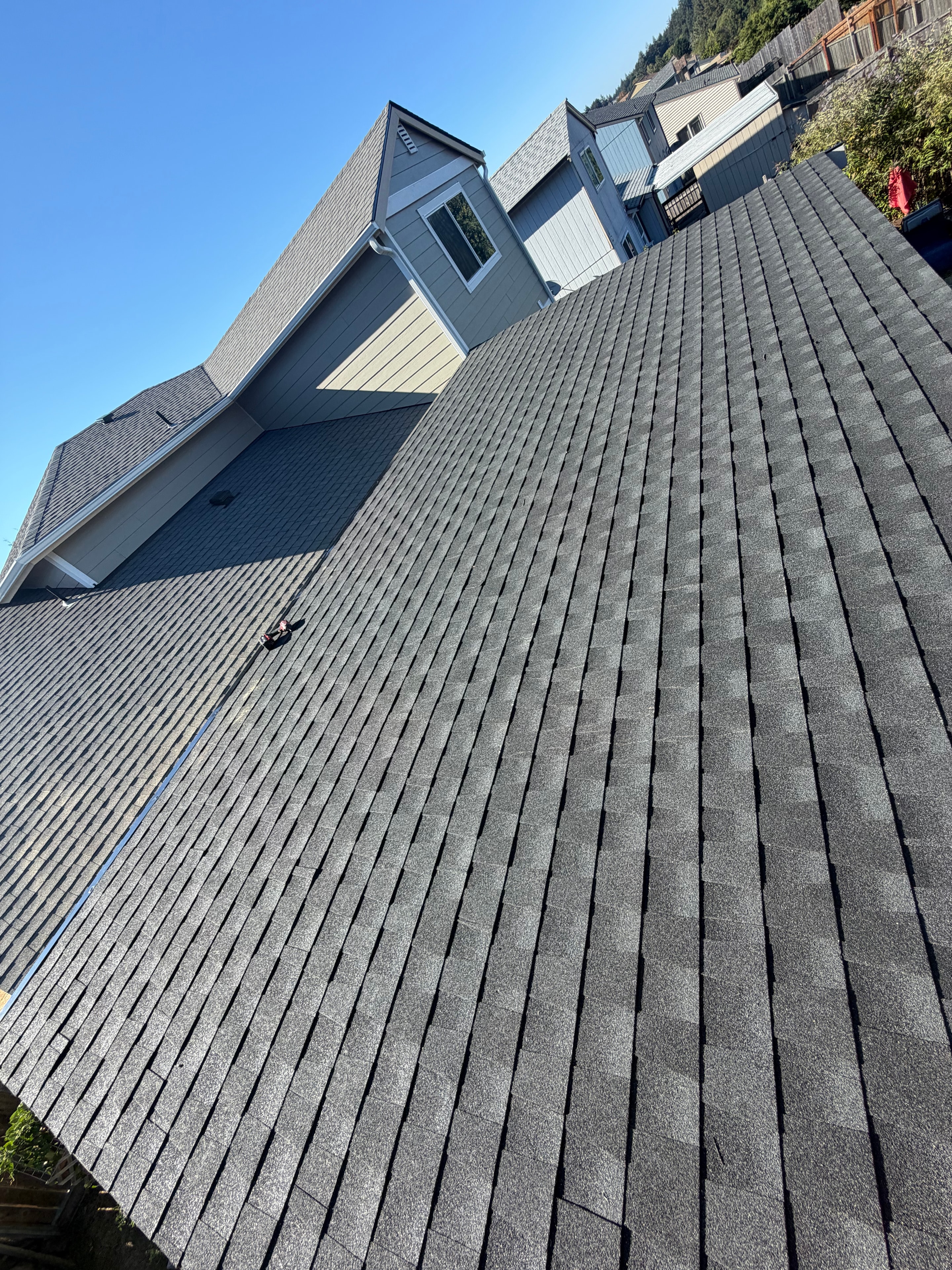 Modern two-story home with dark architectural shingles, blue-grey siding, and attached garage under clear blue sky